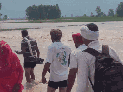 Villagers passing through the water of the Markanda river stored on the road in Kathwa village.