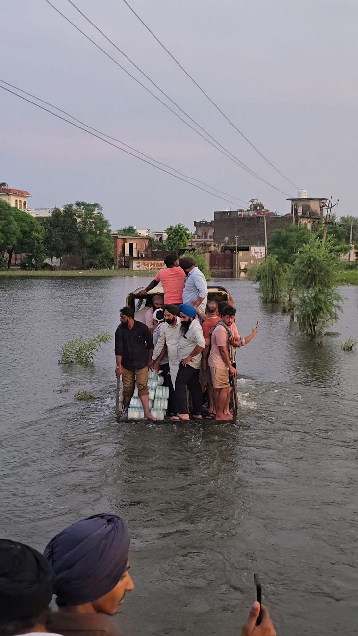 होशियारपुर के डेरा बाबा नानक एरिया के बाढ़ प्रभावित एरिया में पीने वाला पानी और अन्य सामान लेकर जाते हुए लेाग।
