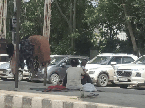 फुटपाथ पर बच्चों के साथ बैठी महिला व रखे कपड़े।