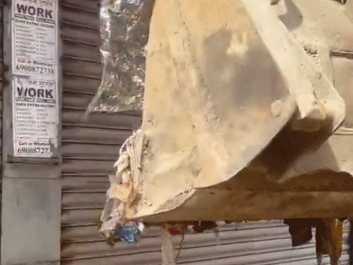 बुलडोजर की मदद से कर्मी दुकान के सामने कुड़ा डालते हुए नजर आते हैं