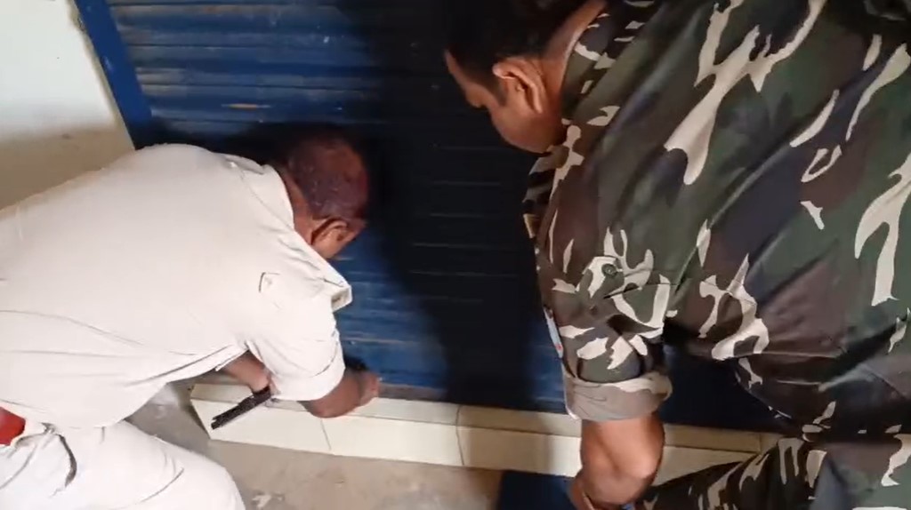 बाहर से लॉक बैंक के शटर को खोलते पुलिसकर्मी।