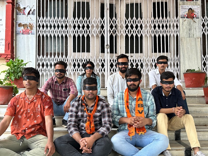 कार्यकर्ता आंखों पर काली पट्टी बांधकर सीढ़ियों पर बैठ गए। जहां 'कुलपति को बर्खास्त करो' और 'कुलपति मुर्दाबाद' जैसे नारे लगाए गए।