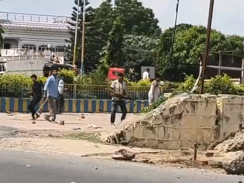 हाथ में राइफल लेकर पत्थर फेंकते लोग।