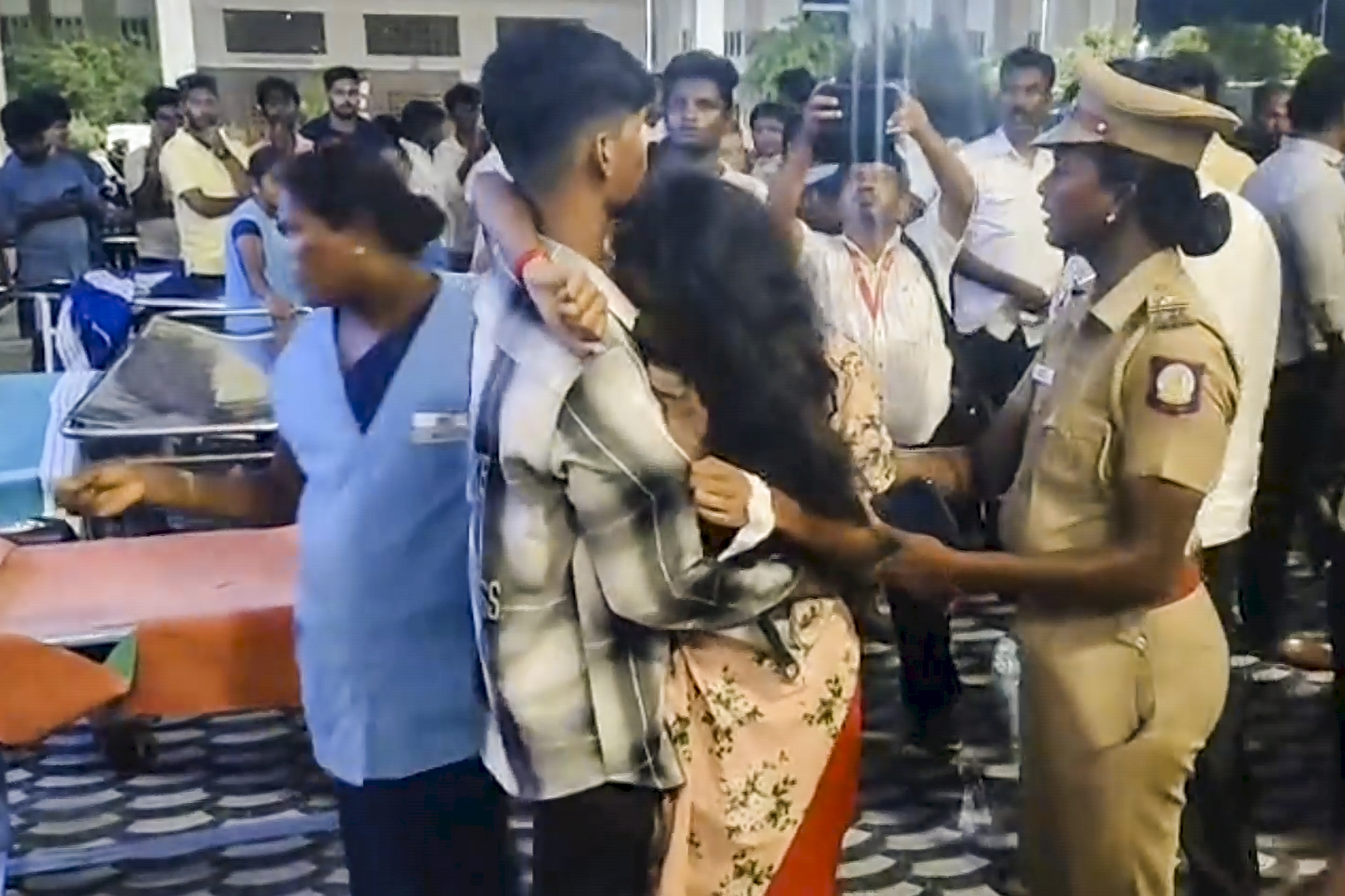 करूर सरकारी रुग्णालयाबाहेर एक महिला तिच्या मुलाला मिठी मारून तिच्या पतीच्या मृत्यूबद्दल शोक व्यक्त करताना