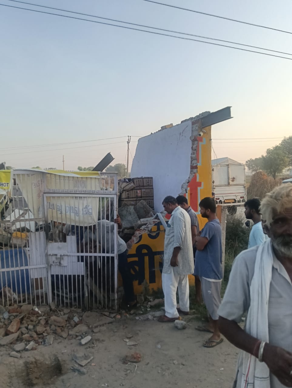 टूटे शराब के ठेके को देखते लोग