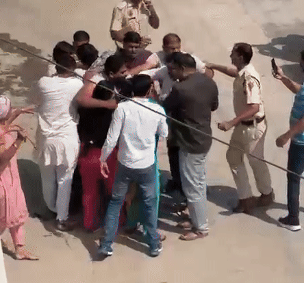 पुलिस पर रबड़ की पाइप से हमला करती हुई गुलाबी सूट पहने हुए महिला।