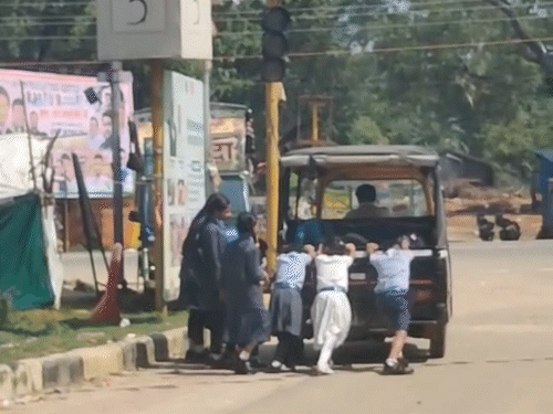 स्कूली बच्चे खराब ऑटो को धक्का लगा रहे हैं।