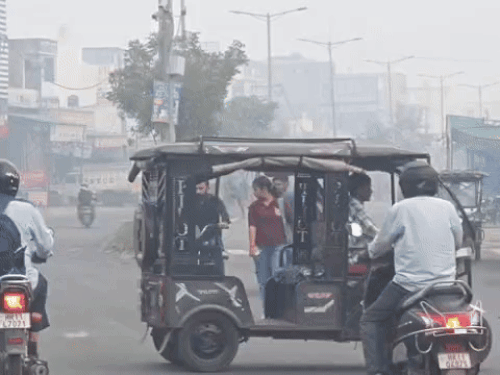 सुबह के समय हल्की धुंध में गुजरते वाहन व राहगीर।