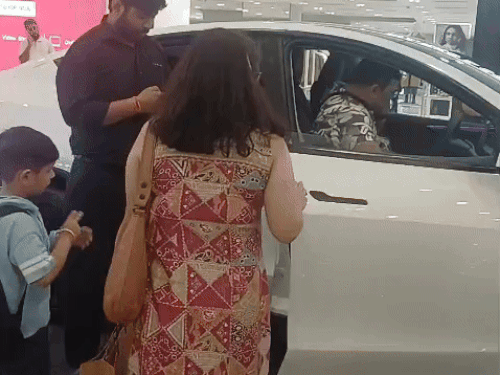 गुरुग्राम के एंबियंस मॉल में खड़ी टेस्ला गाड़ी के फीचर्स चेक करता परिवार।