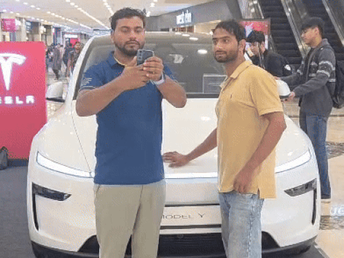 एंबियंस मॉल में खड़ी टेस्ला गाड़ी के साथ सेल्फी लेते युवक।
