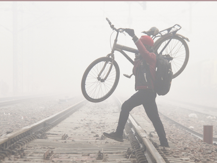 हरियाणा: गुरुग्राम में घने कोहरे के चलते विजिबिलिटी कम हो गई। शख्स साइकिल को उठाकर रेलवे ट्रैक पार कर रहा है।