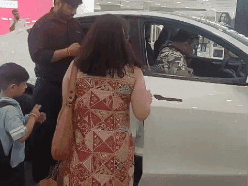गुरुग्राम के एंबियंस मॉल में खड़ी टेस्ला गाड़ी के फीचर्स चेक करता परिवार।
