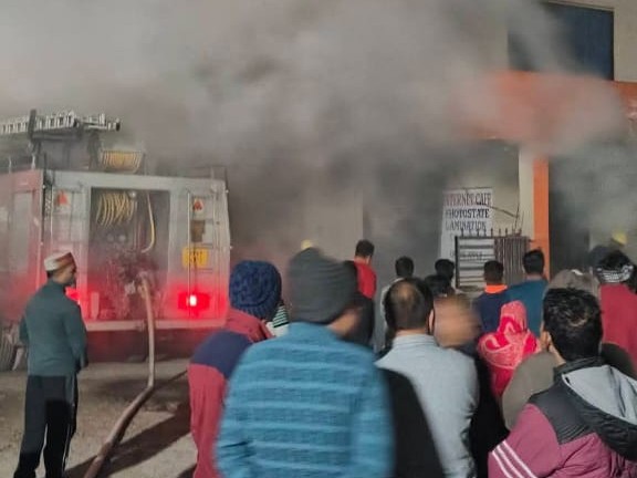 लगी आग को बुझाने में लगी दमकल गाड़ी, खड़े लोग