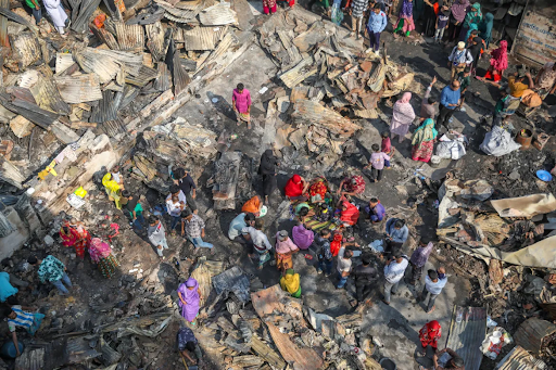 अपने घर के जले हुए अवशेषों को देखते हुए लोग।