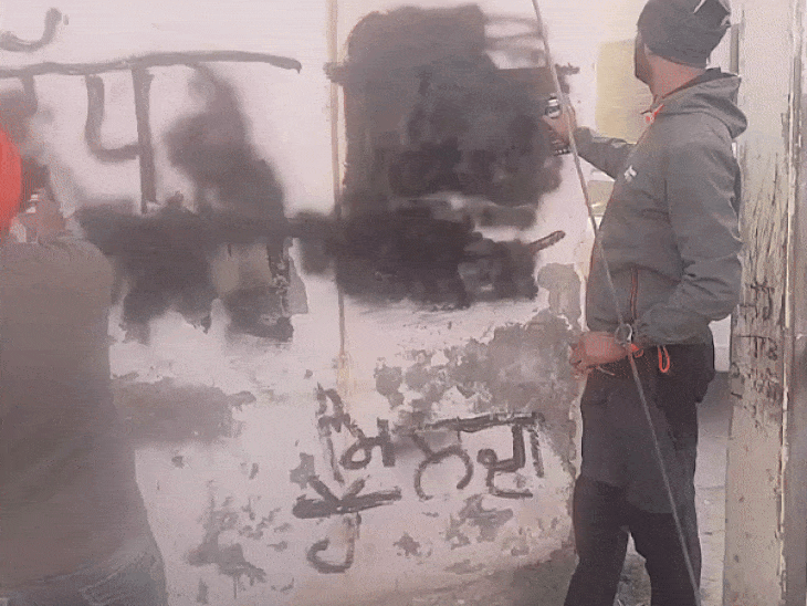 दीवार पर लिखे नशा बिकता है के सलोगन मिटाते हुए कर्मचारी।