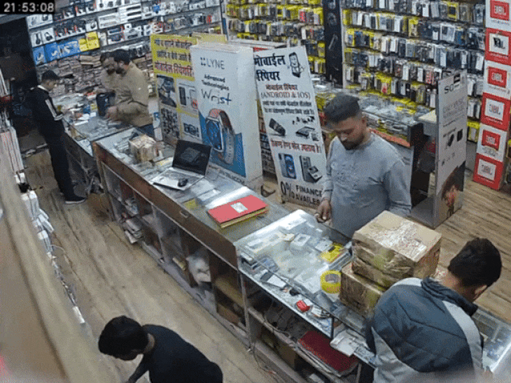 मोबाइल शॉप के अंदर खड़ा सेल्समैन नीचे आयटम खोजने लगा तब युवक काउंटर पर पड़े मोबाइल को अपनी जेब में डाल रहा।