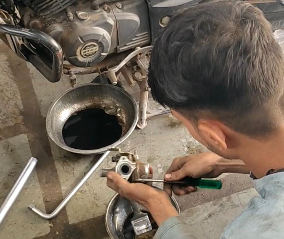 बाइक के कार्बोरेटर को खोलते हुए मैकेनिक