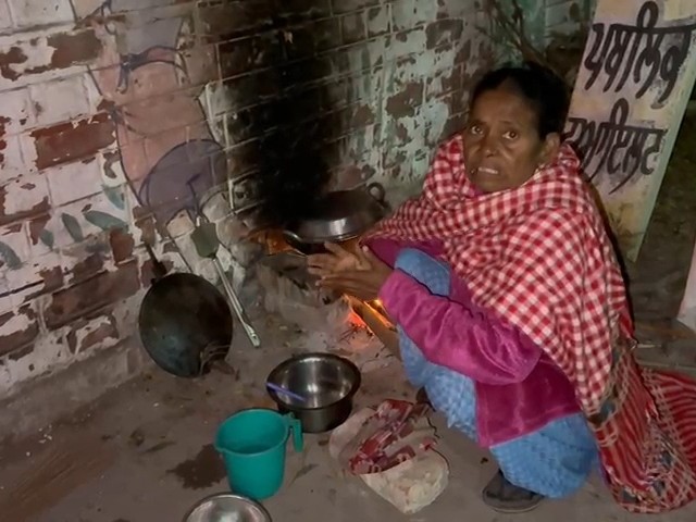 सड़क के किनारे एक दीवार की वोट में खाना बनाती महिला