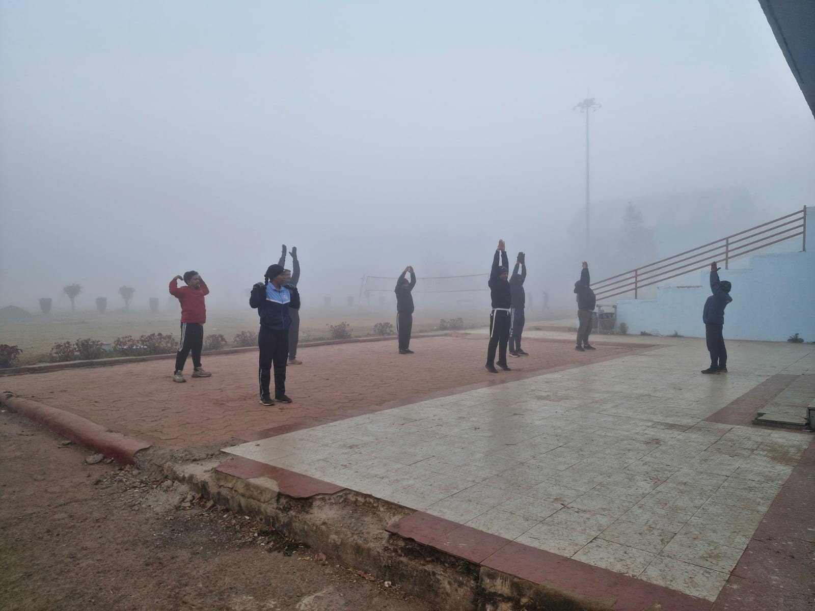 सुबह के वक्त कोहरे के बीच योगा करते लोग।
