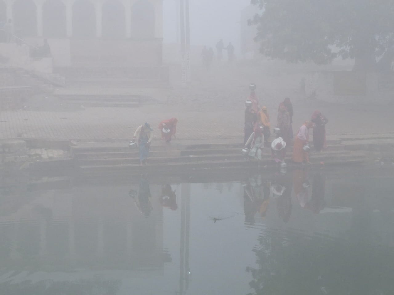 कोहरे के बीच मुंडवा के लाखोलाव तालाब से पानी भर्ती महिलाएं