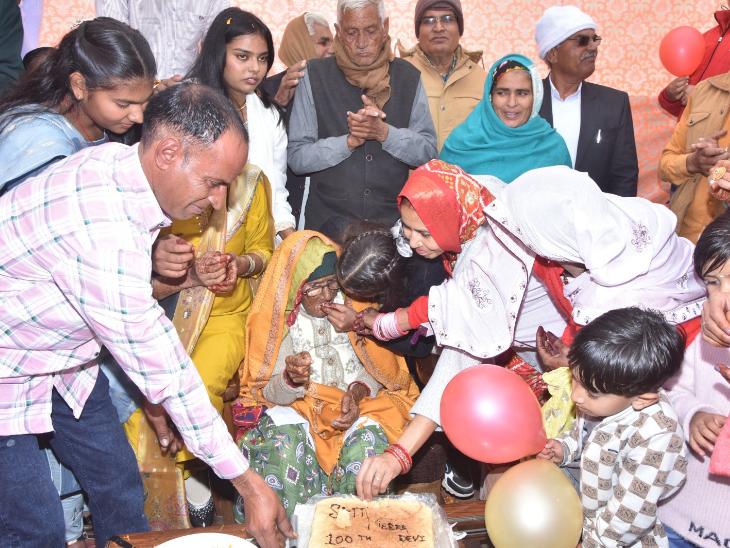 100वें जन्मदिन पर बुजुर्ग मीरा देवी को केक खिलाते परिवार के सदस्य।