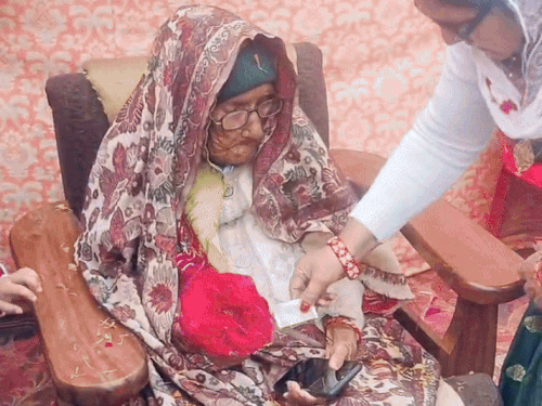 मीरा देवी के पैर छूकर उनसे आशीर्वाद लेती महिला।