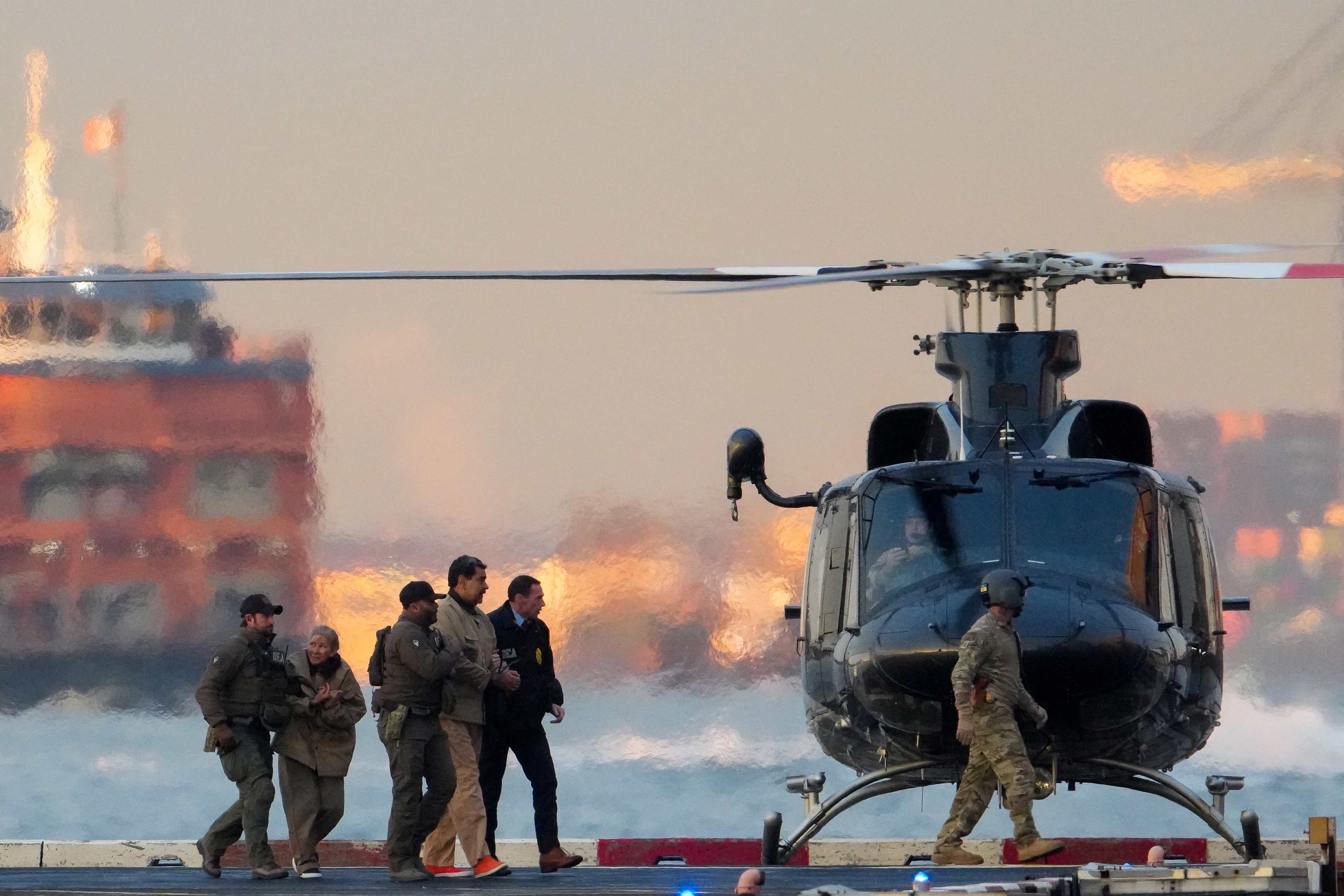 निकोलस मादुरो और उनकी पत्नी सिलिया फ्लोरेस को 5 जनवरी, 2026 को न्यूयॉर्क के डाउनटाउन मैनहट्टन हेलीपोर्ट पर सुरक्षा घेरे में ले जाया जा रहा है।