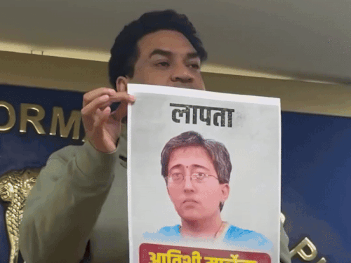 दिल्ली भाजप नेत्या आतिशी विधानसभेत न पोहोचल्याने त्यांचे हरवल्याचे पोस्टर दाखवताना.