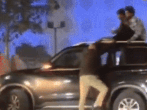 युवक कहने से नीचे नहीं उतरते हैं तो पुलिसकर्मी उन्हें हाथ पकड़कर नीचे उतारने के लिए खुद कार पर चढ़कर उन्हें उतारने की कोशिश करता है।