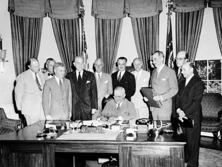 1949 में नाटो एग्रीमेंट पर दस्तखत करते अमेरिकी प्रेसिडेंट हैरी एस ट्रूमैन और उनके पीछे खड़े अन्य 11 नाटो सदस्य।
