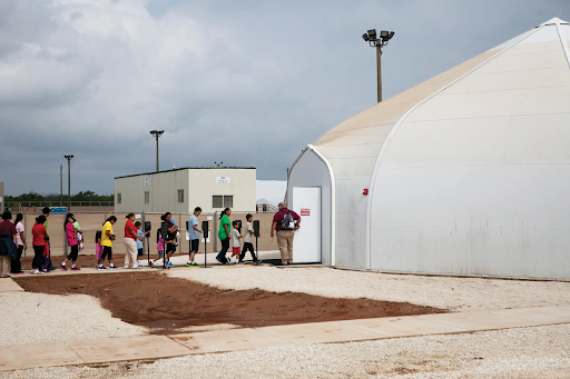 अमेरिका के सबसे बड़े इमिग्रेशन डिटेंशन सेंटर, डिली (टेक्सास) स्थित साउथ टेक्सास फैमिली रेजिडेंशियल सेंटर में बंद लोग खाने के लिए लाइन में खड़े हैं। इनमें कई बच्चे भी हैं।