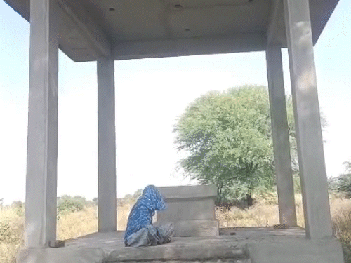 कुम्हारों का बास में शहीद के अधूरे स्मारक पर बैठी वीरांगना विनोद देवी।