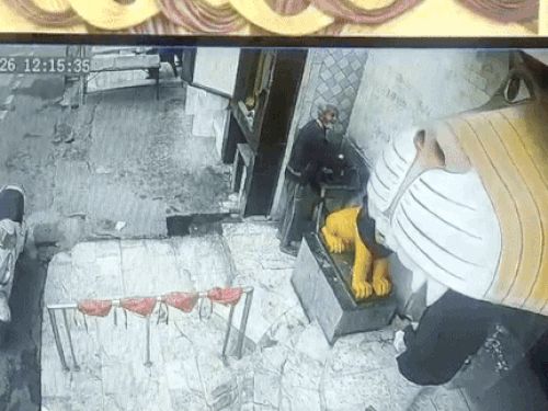 मंदिर के बाहर झूठे बर्तन धो रहा व्यक्ति जिसे श्रद्धालु रोकता हुआ।