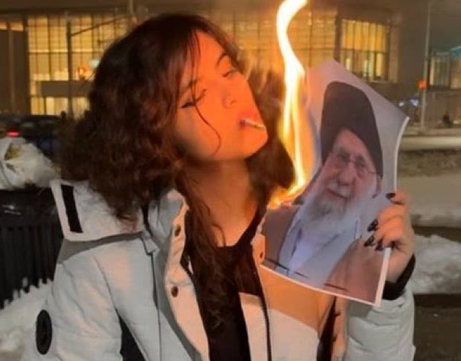 ઈરાની મહિલા સર્વોચ્ચ નેતા અયાતુલ્લા અલી ખામેનેઈની સળગતી તસવીરથી સિગારેટ સળગાવતી વખતે.