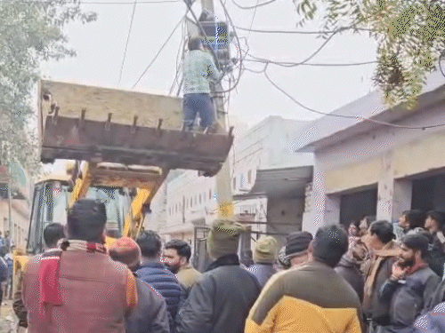 मकान तोड़ते समय जब बिजली के तार बीच में आए, तो कर्मचारियों ने उन्हें हटाया।
