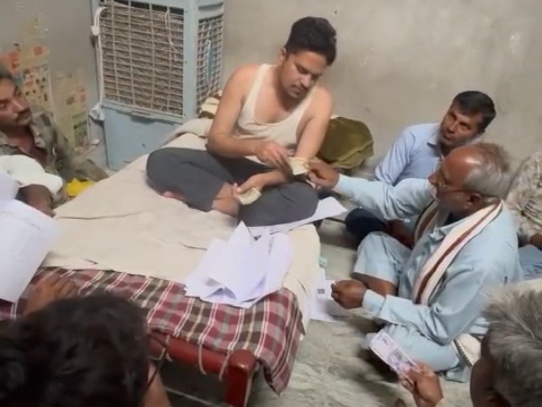 चारपाई पर बैठे पटवारी दिनेश जाणी ग्रामीणों से रुपए लेते हुए।