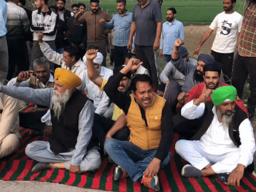 सड़क पर बैठकर पुलिस के खिलाफ नारेबाजी करते किसान।