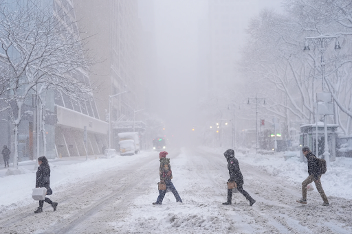 न्यूयॉर्क में बर्फीले तूफान के दौरान स्ट्रीट पार करते पैदल यात्री। सड़क पूरी तरह बर्फ से ढक गई है।