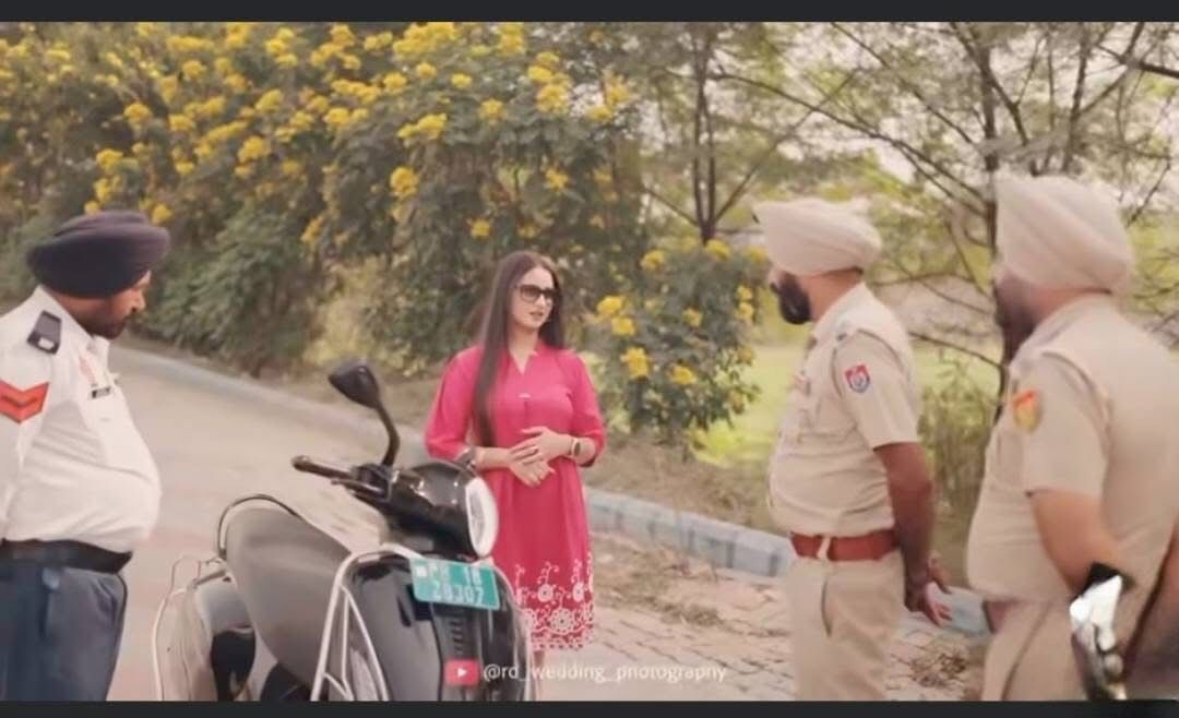 बिना हेलमेट स्कूटी चला रही महिला को मानिक के कहने पर बिना चालान काटे छोड़ते पुलिसकर्मी। सभी पीछे हाथ कर खड़े हैं।