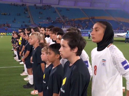 ईरानी महिला टीम ने सोमवार रात एशियाई महिला फुटबॉल कप के उद्घाटन मैच में अपना राष्ट्रीय गान नहीं गाया। खिलाड़ी लाइन में खड़ी थीं, लेकिन गान के दौरान सिर्फ सामने देखा और चुप रहीं। टीम की कोच मारजियेह जाफरी भी अपनी खिलाड़ियों की चुप्पी देख मुस्कुरा रही थीं। यह कदम हाल के अमेरिका-इजराइल हमलों और ईरान के नेताओं की मौत के बीच एक विरोध का संदेश माना जा रहा है।