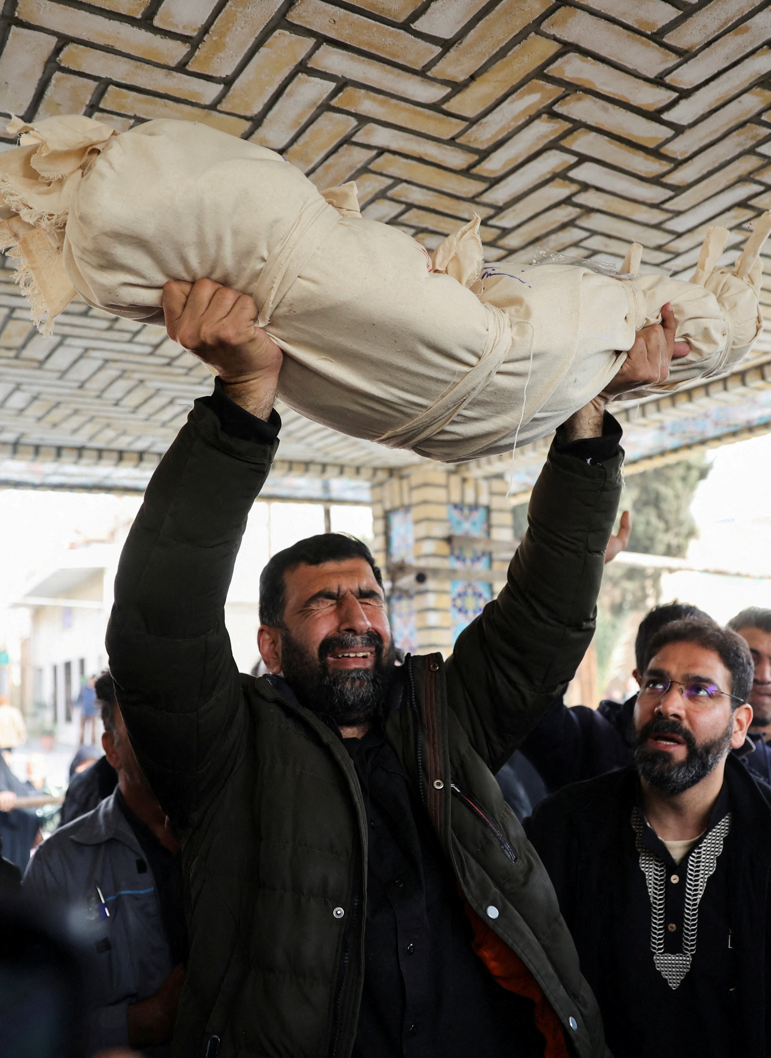 तेहरान में अमेरिकी-इजराइली हमले में मारी गई 2 साल की जैनब साहेबी के अंतिम संस्कार में एक आदमी शव हाथ में उठाकर रोते हुए।