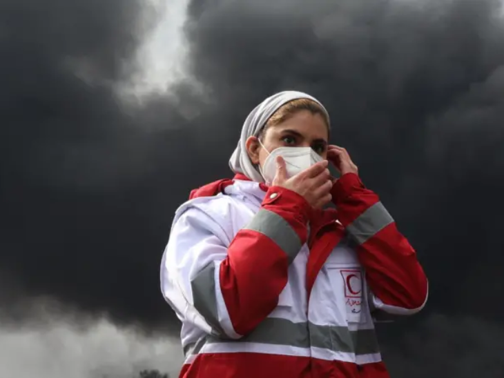 ईरान के शाहरान में तेल रिफाइनरी पर हमले के बाद रेड क्रिसेंट सोसाइटी की एक महिला सदस्य मास्क पहने हुए है।