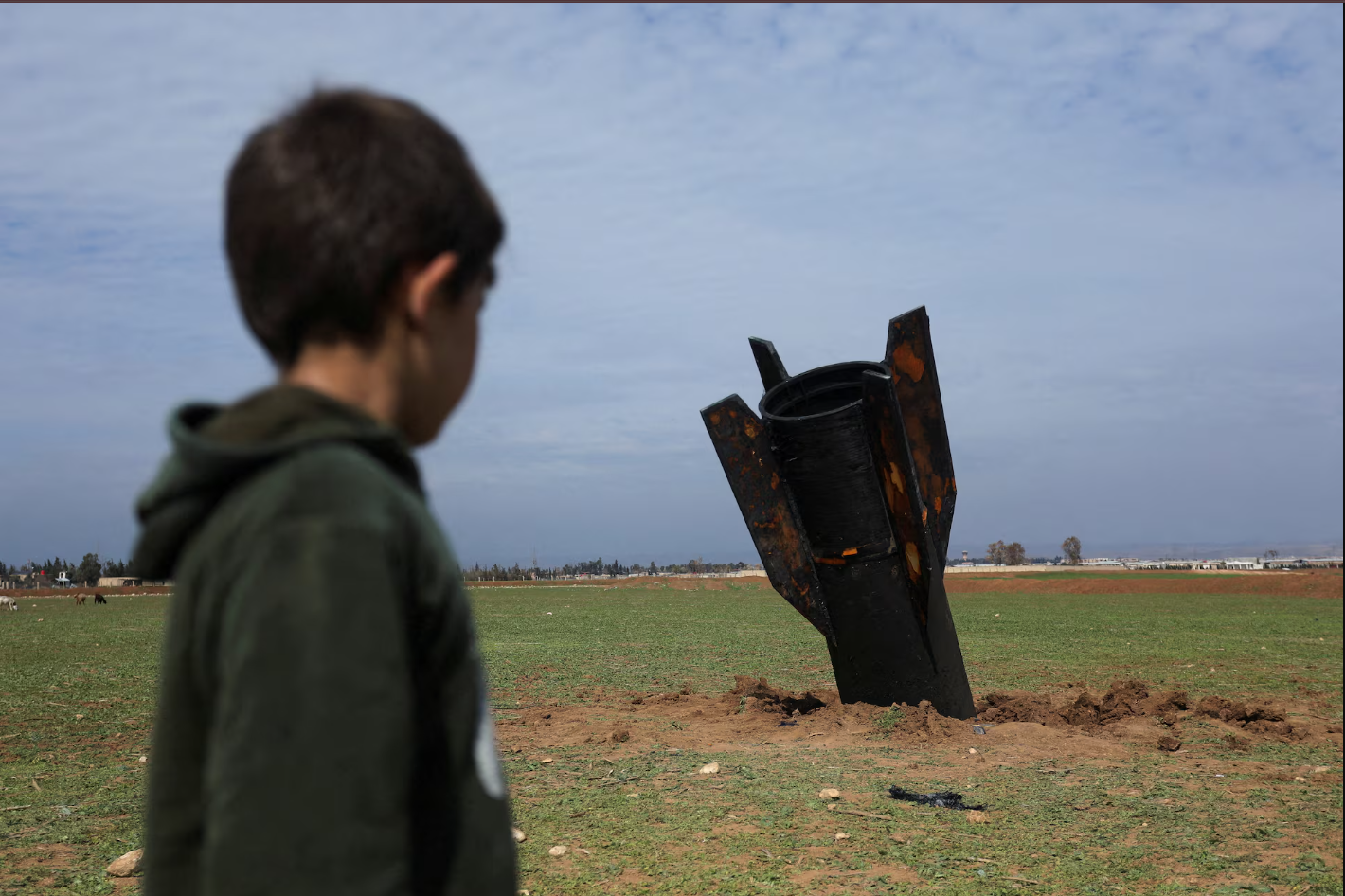 सीरिया के कामिशली में ईरान के साथ अमेरिका-इजरायल संघर्ष के बीच, कामिशली इंटरनेशनल एयरपोर्ट के पास गिरी मिसाइल को एक बच्चा देखता हुआ।