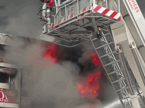 क्रेन पर चढ़कर आग बुझाते दमकल कर्मचारी।