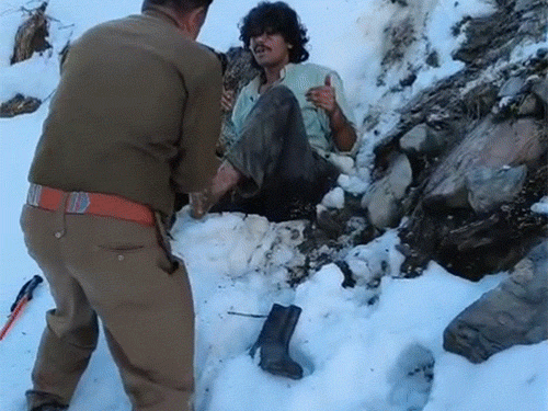 बर्फ में फंसे ट्रैकर को जूते पहनाते हुए पुलिस जवान।
