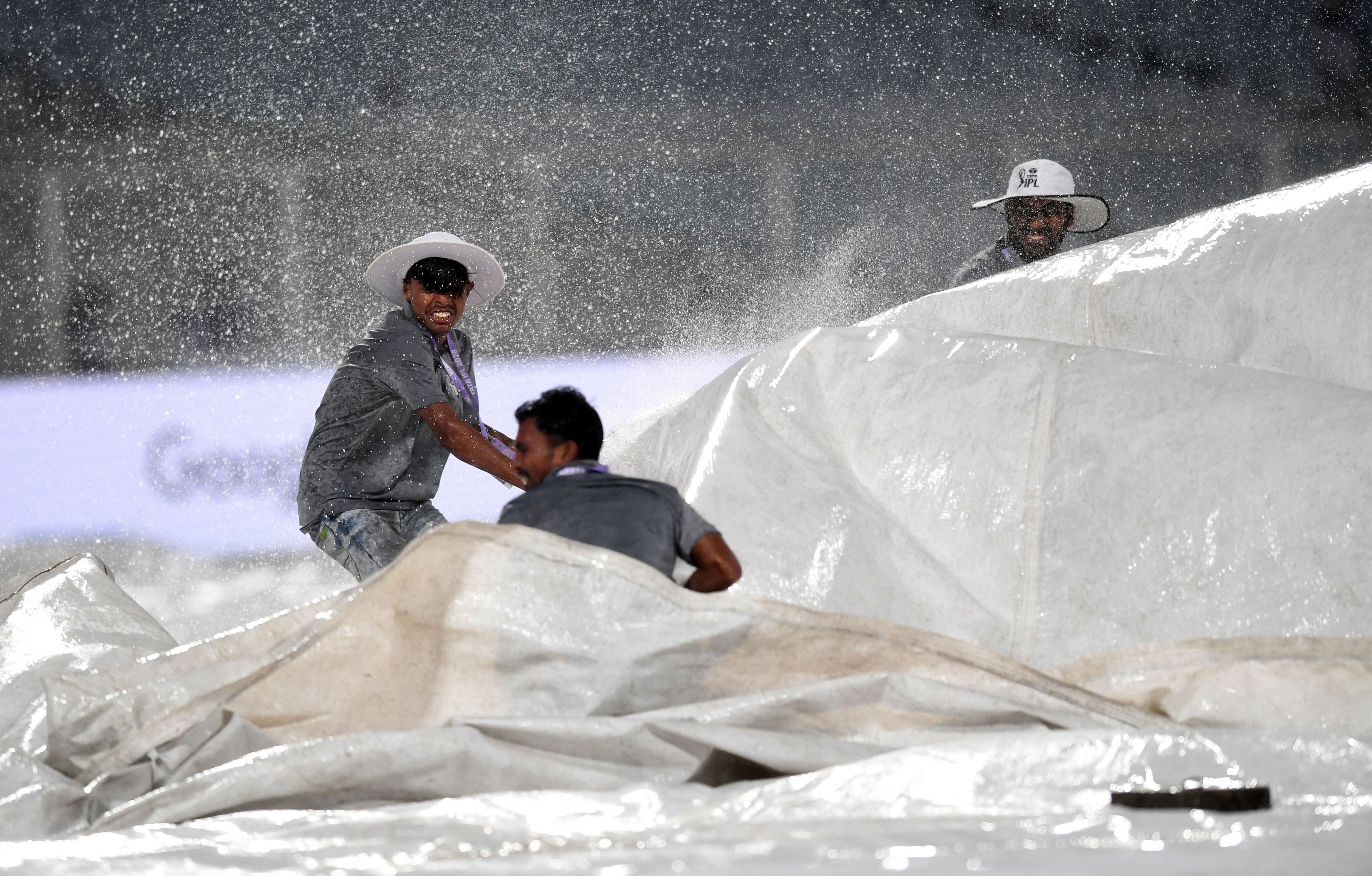 बारिश के कारण मैदान को कवर करता ग्राउंड स्टाफ।