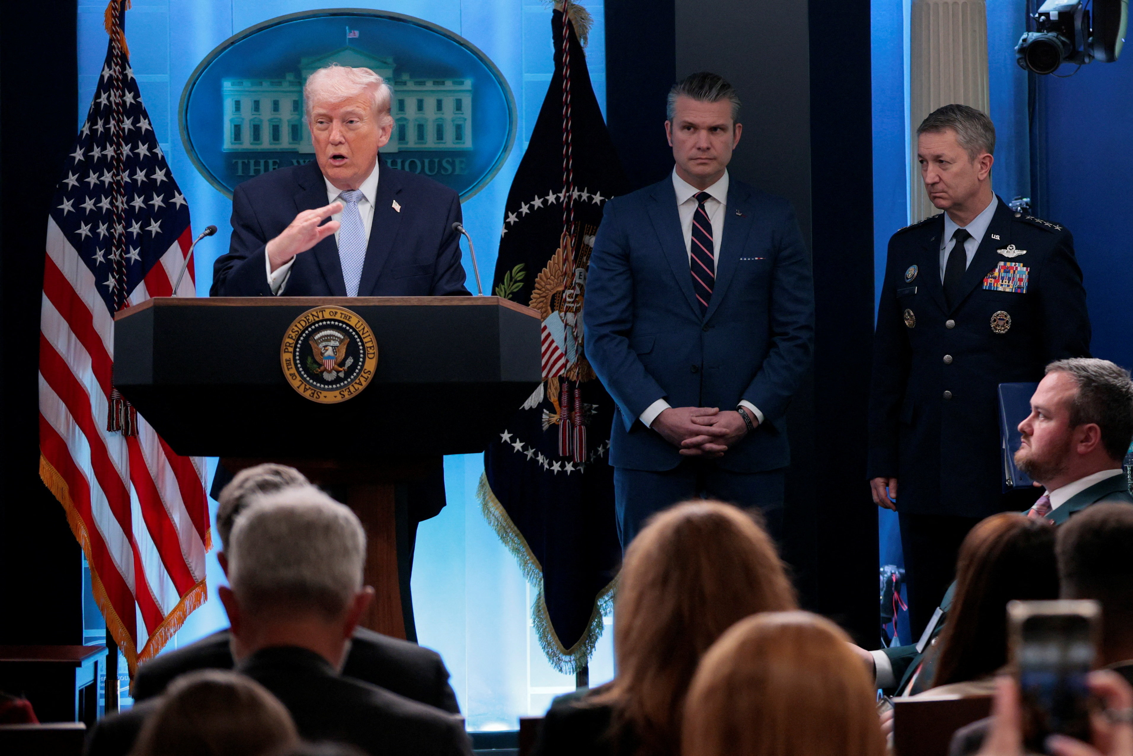 ट्रम्प के संबोधन के दौरान उनके बाए रक्षा मंत्री पीट हेगसेथ और सबसे दाएं जॉइंट चीफ्स के चेयरमैन जनरल डैन केन।