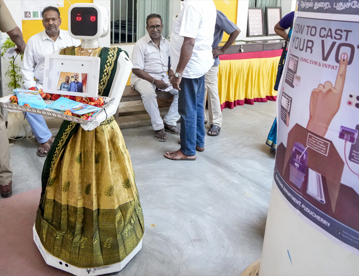 पुडुचेरी में मतदान केंद्र पर रोबोट ने मतदाताओं का फूलों से स्वागत किया।