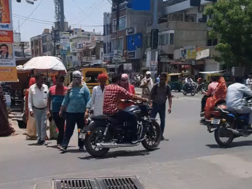 दोपहर के समय तेज धूप है, इसलिए लोग सिर ढककर चल रहे हैं।