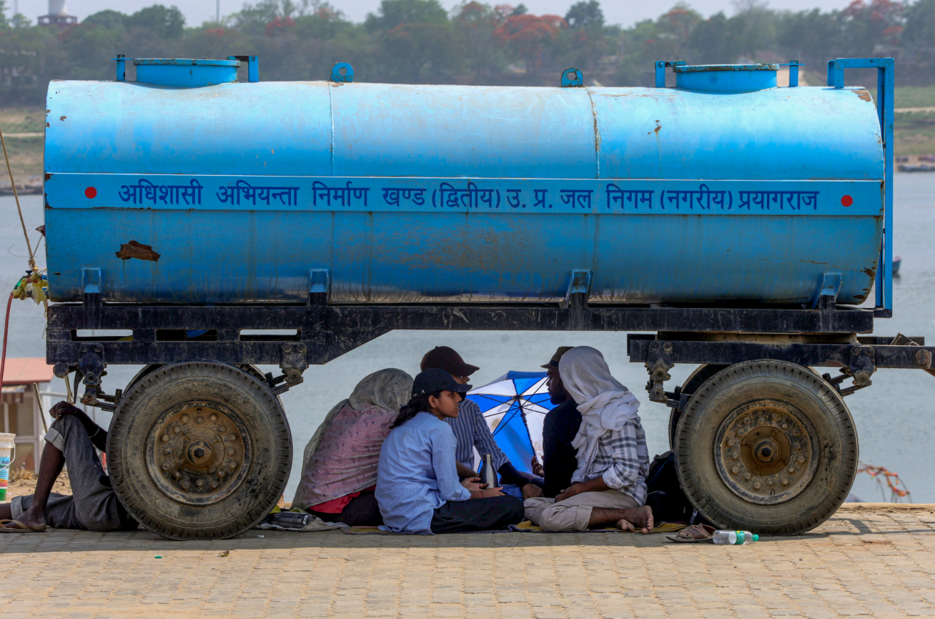 उत्तर प्रदेश के प्रयागराज में भीषण गर्मी के बीच लोग पानी के टैंकर के नीचे छांव में बैठे दिखे।